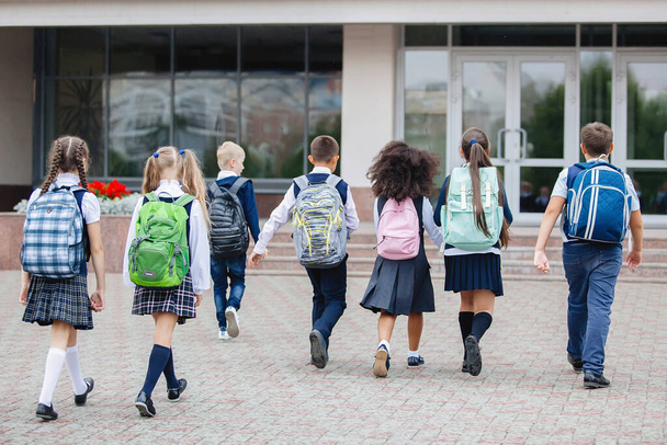Учні в уніформі і з рюкзаками йдуть до школи
. - Фото, зображення