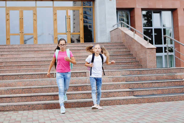 Две школьницы с рюкзаками выбегают из школы после урока. - Фото, изображение