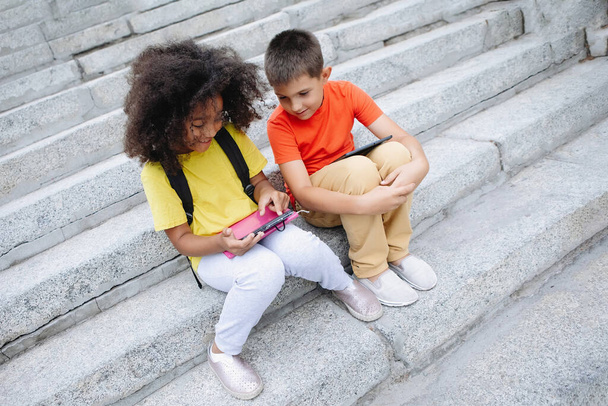Due adolescenti, un ragazzo e una ragazza africana, sono seduti sui gradini con uno smartphone in mano
. - Foto, immagini