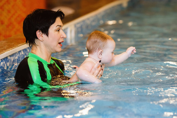 Woman child trainer and toddler swim and study in blue water pool - Photo, Image