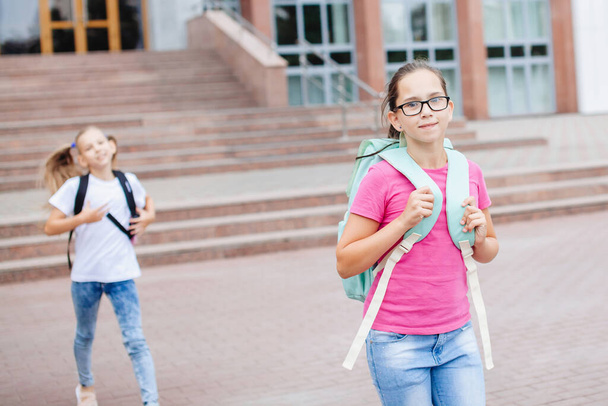 Dvě školačky s batohy vyběhnou po vyučování ze školy. - Fotografie, Obrázek