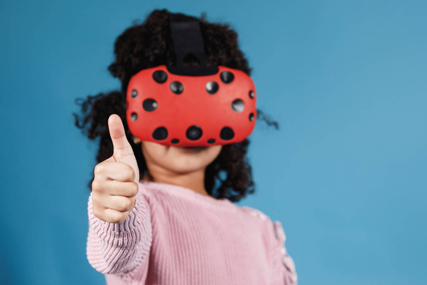 Afro-Amerikaans meisje speelt met virtual reality brillen. Computerspelletjes, blauwe achtergrond, emoties. - Foto, afbeelding