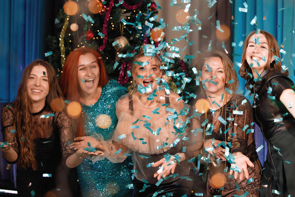 Group of friends celebrates the New Year with confetti near the Christmas tree. People laugh and rejoice. - Photo, Image