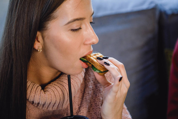 Woman eats a sandwich in a cafe. Close-up. - 写真・画像