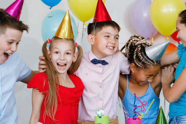 Enfants lors d'une fête d'anniversaire avec boules, casquettes, bonbons et rires. - Photo, image
