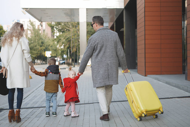 Turistien perhe, isä, äiti, tytär ja poika keltaisella matkalaukulla tulevat hotelliin
. - Valokuva, kuva