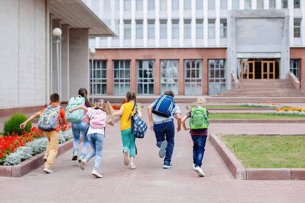 Grupa uczniów z plecakami biegnie do szkoły na lekcje. Widok z tyłu. - Zdjęcie, obraz