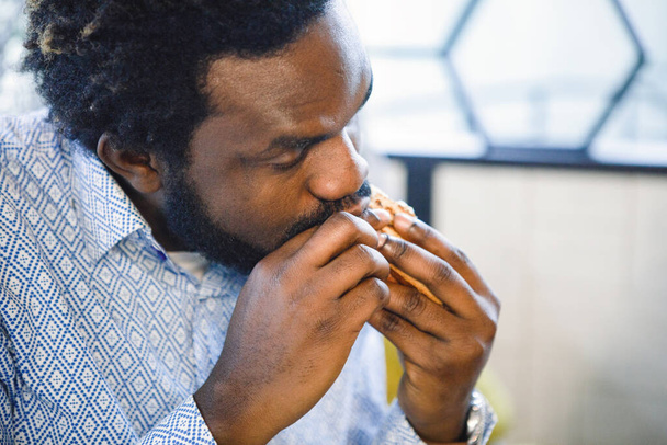African man eats a sandwich in a cafe. Close-up. - Фото, зображення