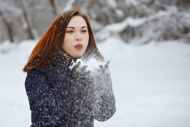 Mujer joven y bonita en una bufanda azul y chaqueta con largos golpes de pelo en la nieve en sus manos al aire libre en un bosque cubierto de nieve. Juventud, belleza, estilo de vida saludable, sueños
. - Foto, imagen