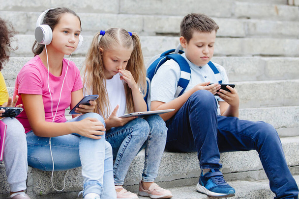 Group of schoolchildren of different nationalities, in colorful clothes sitting on stone steps. Teenagers talking, listening to music on headphones, reading books. - Valokuva, kuva