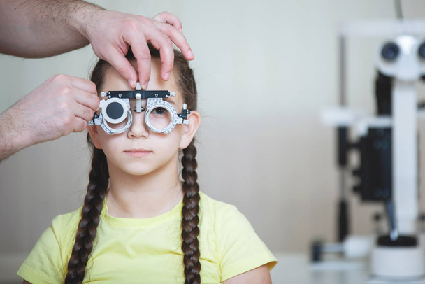 Badanie wzroku przez okulisty okulary testowe ramki dla nastolatek dziewczyna w żółtym t-shirt z warkocze. - Zdjęcie, obraz