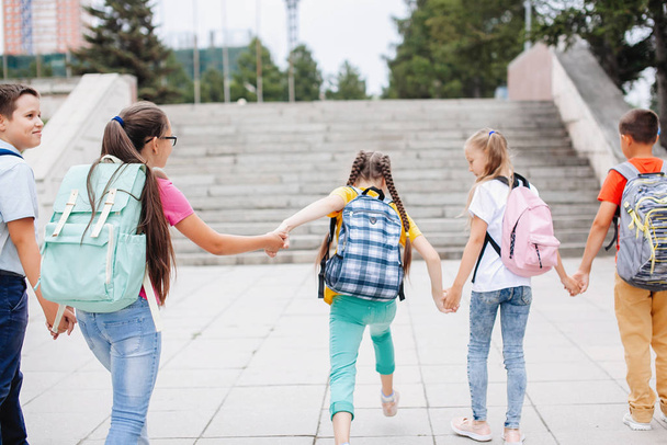 Дети-подростки в разноцветной одежде с рюкзаками идут по лестнице в школу. Вид сзади. - Фото, изображение
