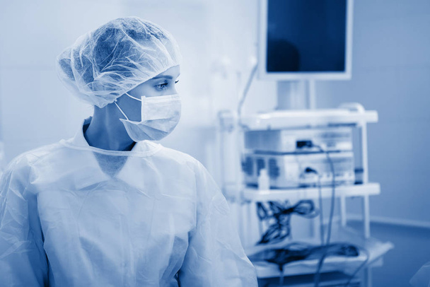 Műtéti nővér egyenruhában, maszkban és sapkában. A monitor hátterében. - Fotó, kép
