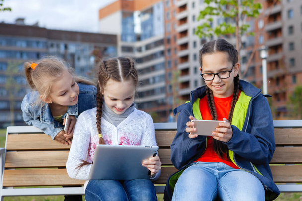 Tre adolescenti con uno smartphone si siede su una panchina in un parco estivo della città. - Foto, immagini