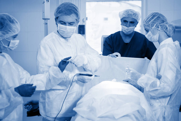 Kirurgi, nukutuslääkäri ja sairaanhoitaja leikkauksen aikana leikkaussalissa
. - Valokuva, kuva