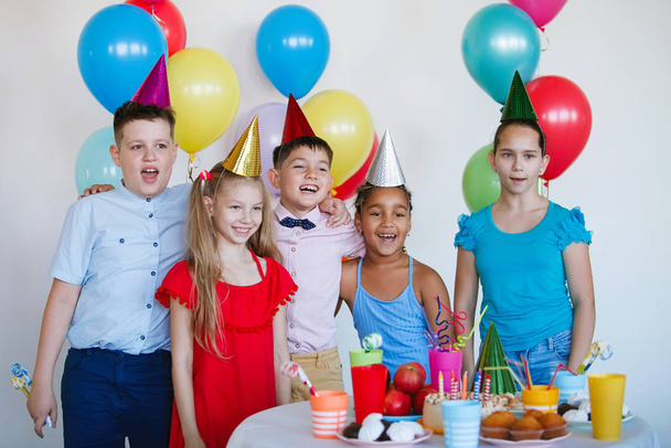 Los niños en una celebración de cumpleaños con bolas, gorras, dulces y risas. - Foto, Imagen
