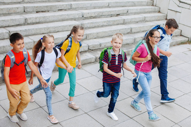 Παιδιά έφηβοι με πολύχρωμα ρούχα με σακίδια ανεβαίνουν τις σκάλες για το σχολείο. - Φωτογραφία, εικόνα