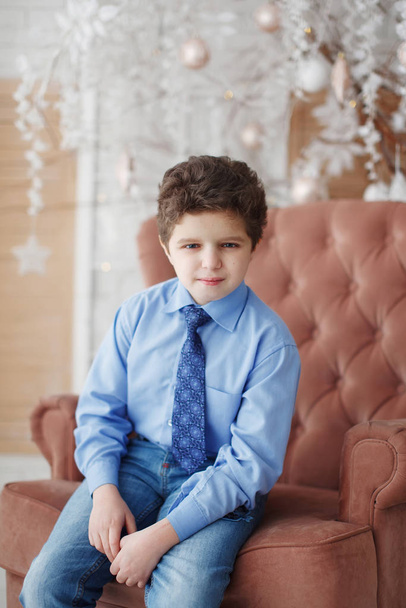 Teen boy in a blue shirt with a tie sitting on a chair - Фото, зображення