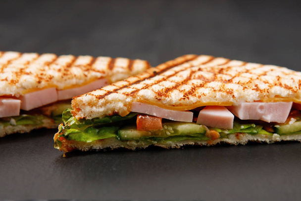 Треугольный домашний сэндвич на плоской тарелке. Тост, салат, курица, помидоры на черном столе. - Фото, изображение