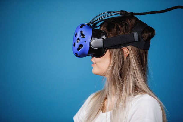 Mladá žena s brýlemi ve virtuální realitě, portrét zblízka. Počítačové hry, modré pozadí, emoce. - Fotografie, Obrázek