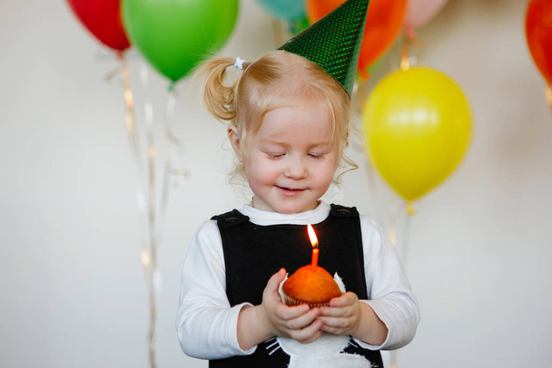 キャップの女の子はケーキの上に誕生日のろうそくを吹きます - 写真・画像