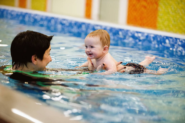 Woman child trainer and toddler swim and study in blue water pool - Foto, imagen