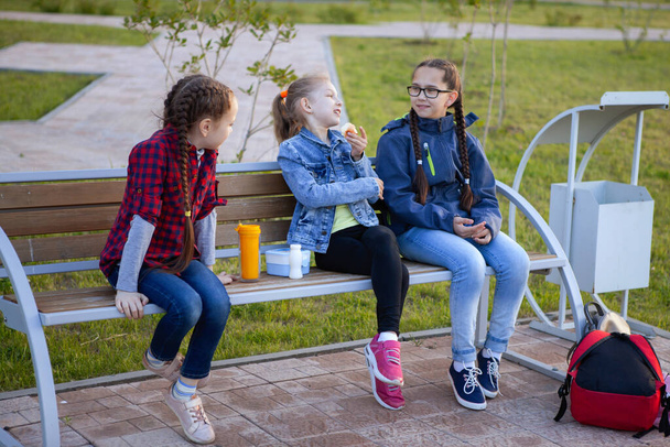 Les adolescentes mangent sur un banc dans un parc de la ville. Nourriture saine, boîte à lunch. Les gens, les enfants, les amis et le concept d'amitié
. - Photo, image
