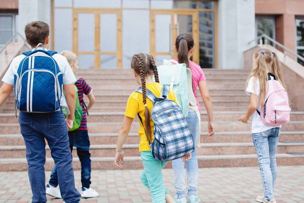 Eine Gruppe von Schulkindern mit Rucksäcken läuft die Treppe zur Schule hinauf, um dort Unterricht zu nehmen. Rückseite. - Foto, Bild