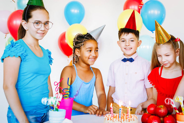 Los niños en una celebración de cumpleaños con bolas, gorras, dulces y risas. - Foto, imagen