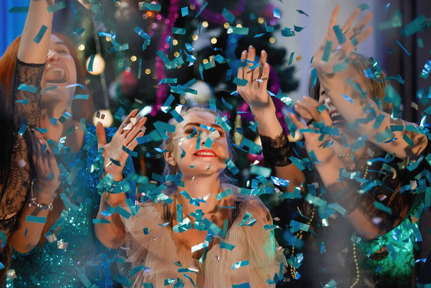Група друзів святкує Новий рік з конфетті біля ялинки. Люди сміються і радіють. - Фото, зображення