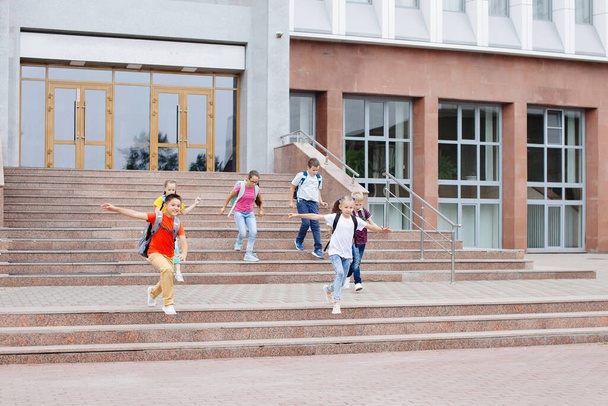 Група школярів з рюкзаками біжить нагору зі школи після уроку
. - Фото, зображення