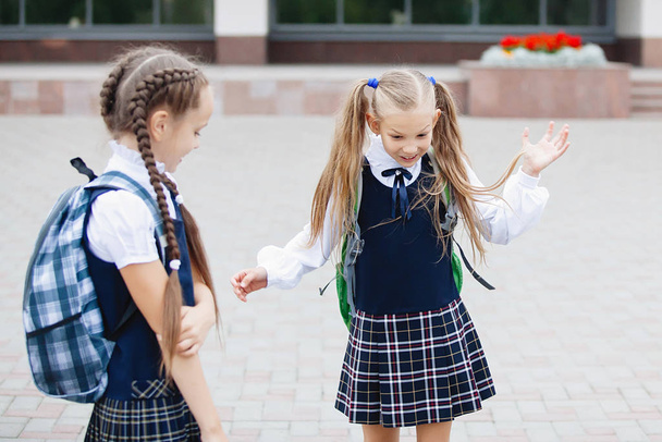 Két iskoláslány kockás szoknyában, iskolai egyenruhában kommunikál órák után egy napos nyári napon a szabadban.. - Fotó, kép