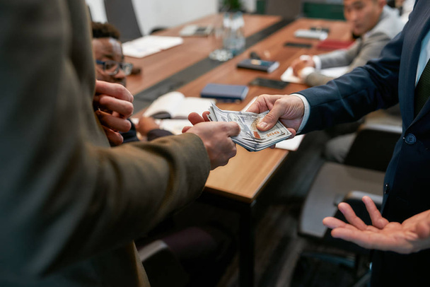 Photo recadrée d'un homme d'affaires donnant de l'argent à son partenaire tout en ayant une réunion dans le bureau moderne
 - Photo, image