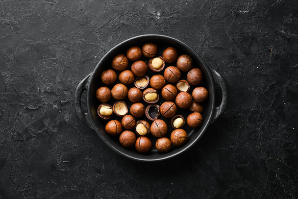 Macadamia nut in bowl on black stone background. Top view. Free space for your text. - Фото, изображение