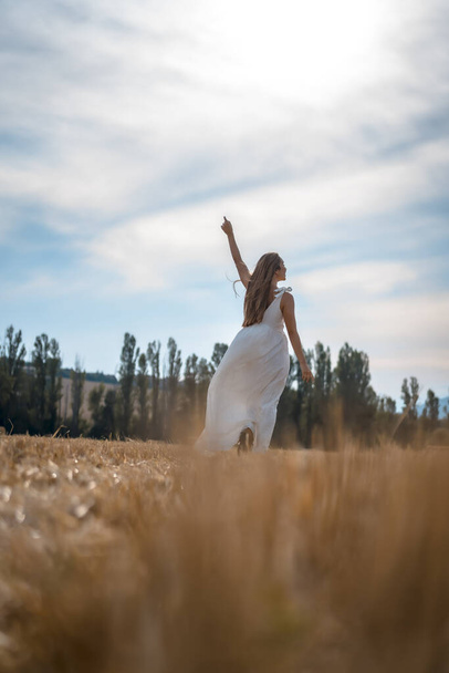 portrait of beautiful young woman wearing white dress in rural field - Photo, image