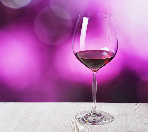 glas rode wijn op paarse achtergrond - Foto, afbeelding