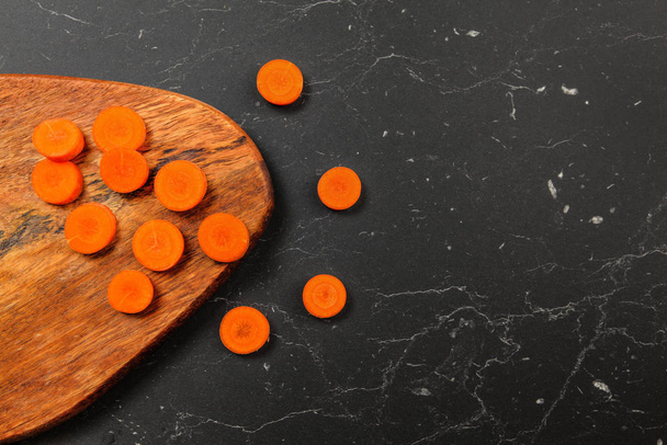 Tabletop view, carrot sliced to small circles on a chopping board, some on black marble next - Zdjęcie, obraz