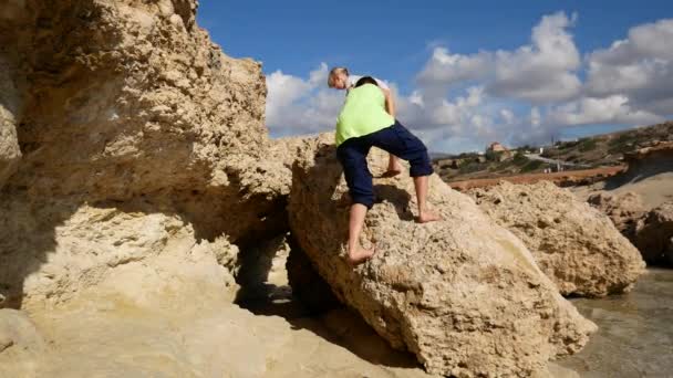 Anya és a baba másznak a sziklák le a Földközi-tenger partján. Ciprus. - Felvétel, videó