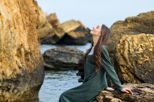 carino giovane ragazza caucasica in abito classico verde rilassante sulla spiaggia vicino a grandi pietre gialle
 - Foto, immagini