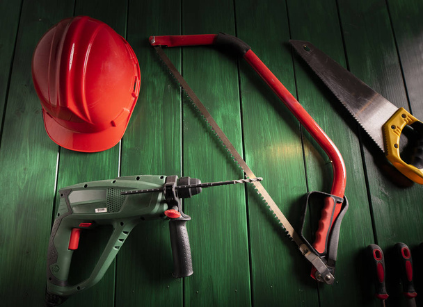Ηλεκτρικό τρυπάνι και κόκκινο προστατευτικό κράνος, εργαλεία κατασκευής και εξοπλισμός εργασίας σε κοντινό πλάνο  - Φωτογραφία, εικόνα
