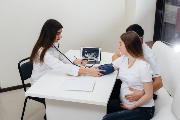 Az orvos egy terhes lány nyomását méri a klinikán. Terhesség és egészségügyi ellátás - Fotó, kép