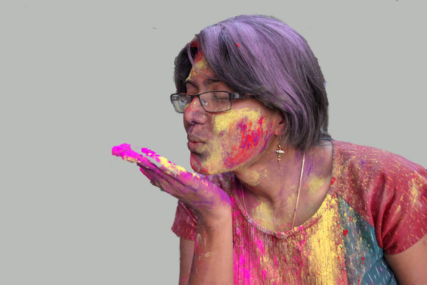 portrait of a young lady with holi colours on face blowing a flying kiss with isolated solid grey background - Photo, Image