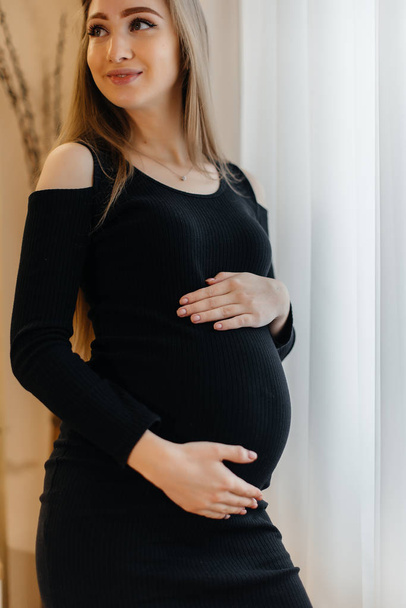 A beautiful pregnant girl is standing in a room near the window - Foto, afbeelding