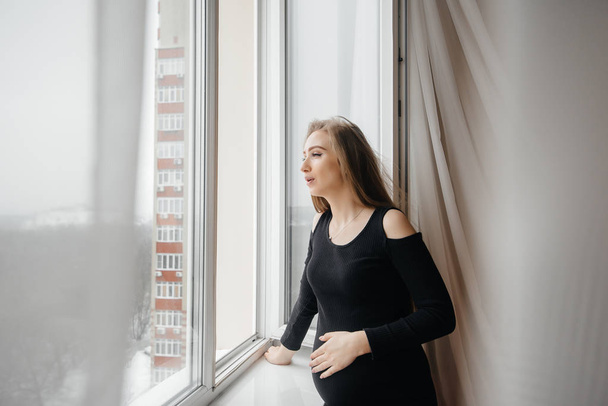 A pregnant girl is breathing fresh air from the window - Fotoğraf, Görsel