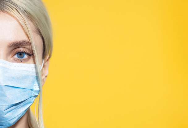 Close-up portret van jong blond meisje dragen medische griep masker op de achtergrond van gele kleur met kopieerruimte. - Foto, afbeelding