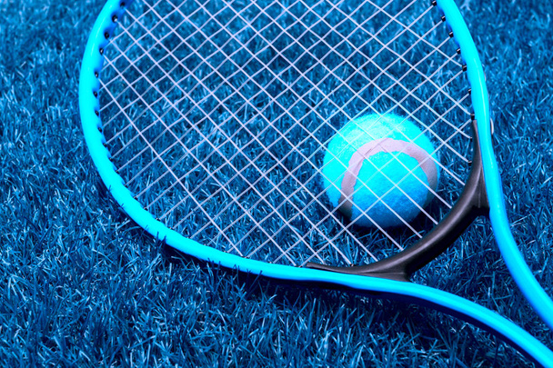 Tennis racket and ball on blue grass. Blue filter - Photo, Image
