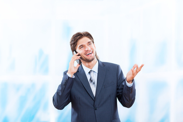 Businessman talking on mobile phone in bright blue office - Zdjęcie, obraz