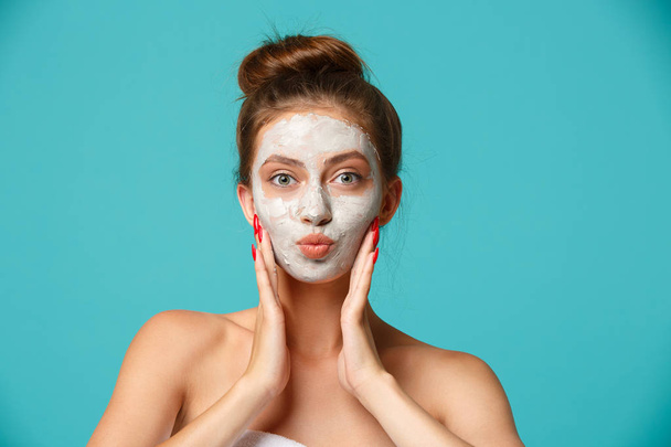 Young woman with towel wrapped around her body applying clay face mask and having fun. Daily morning routine - facial cleaning, skin care, peeling, moisturising and beauty treatment concept - Photo, Image