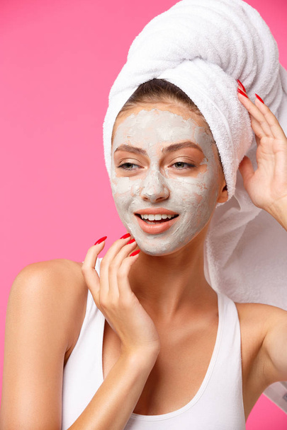 Young woman with towel wrapped around her head applying clay face mask and having fun. Daily morning routine - facial cleaning, skin care, peeling, moisturising and beauty treatment concept - Photo, Image