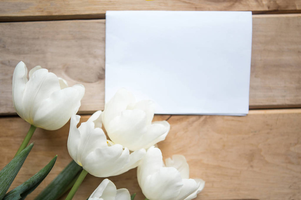 Bouquet of white tulips and white mockup blank on wooden background. Easter or Mother's Day greeting card - Foto, imagen